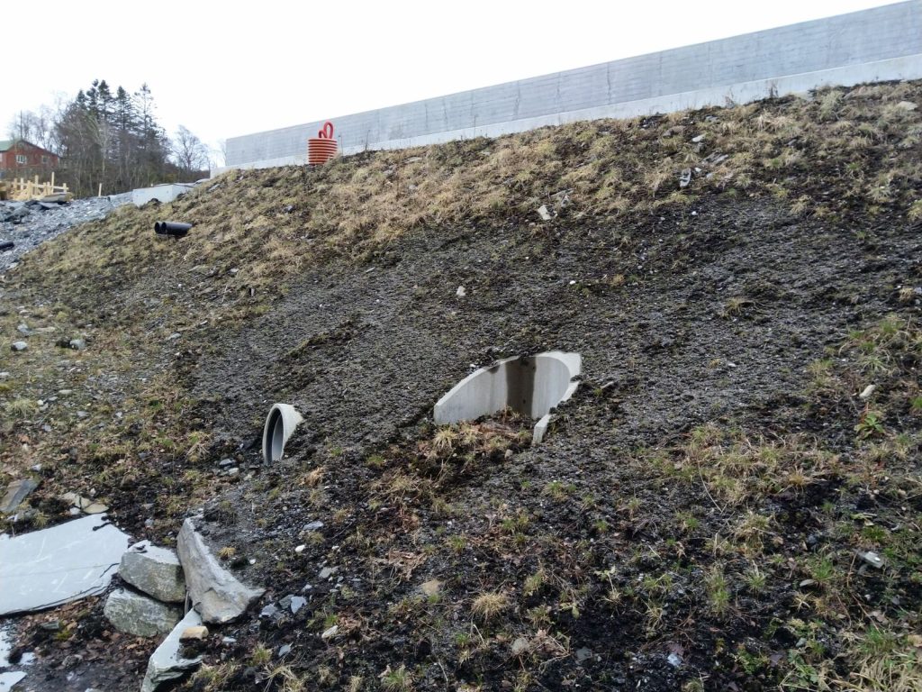 Eiendom berørt av vann- og avløpsinfrastruktur. Skråning med jord, og rør stikkende ut ulike steder.